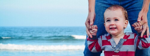 Ein kleines Kind läuft an der Hand der Eltern am Strand entlang.