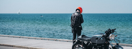 Ein Motorradfahrer steht an einer Straße am Meer.